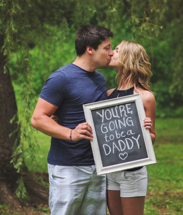 Sesion de fotos pareja besándose con un letrero que dice VAS A SER PAPÁ