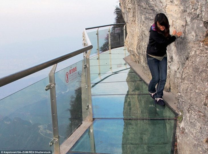 muchacha asustada arriba de un puente transparente