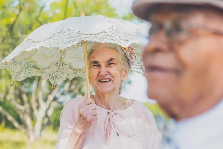 anciana con una sombrilla sonriendo detrás de un anciano