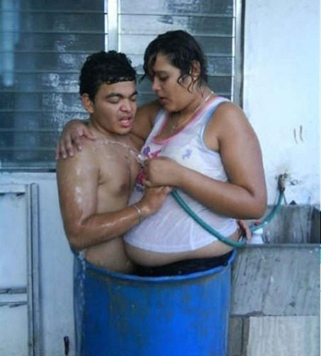 Hombre y mujer adentro de un tambo de basura mojándose con una manguera