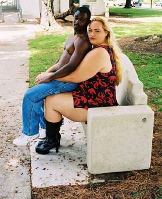 Mujer muy alta junto a hombre muy chico, el esta sentado encima de ella
