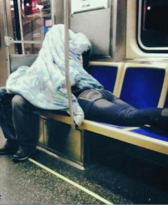 Hombre sentado y mujer acostada boca abajo en el metro tapados por una cobija