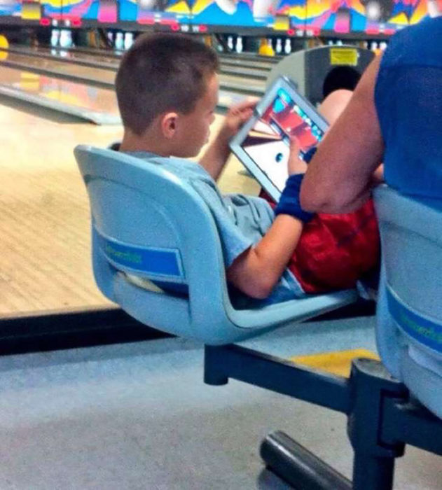 niño jugando boliche en su tableta electrónica en un establecimiento de boliche