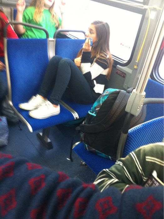 mujer en el autobus ocupando dos lugares con los pies arriba del asiento acojinado