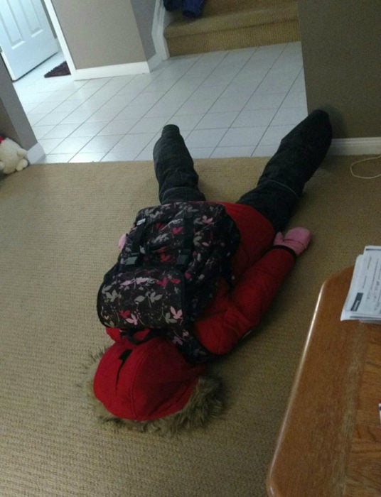 Niña con sudadera roja cansada tirada en el piso de su casa