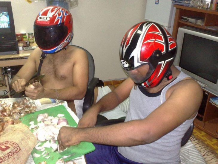 Dos hombres con casco de motociclistas mientras cortan cebolla