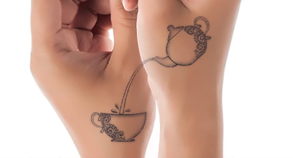 Tatuaje en una mano de una tetera sirviendo café y en la otra mano de la taza de café donde está cayendo