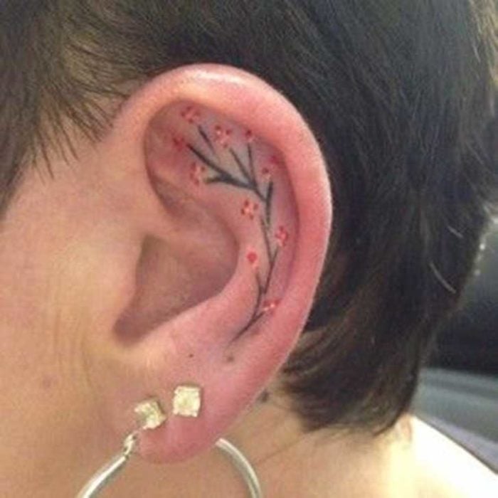 Tatuaje de una rama de un árbol con flores rojas adentro del oído