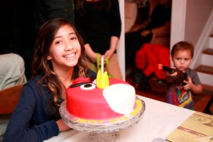 niña sonriendo con su pastel mientras su hermano le apunta con una pistola de juguete