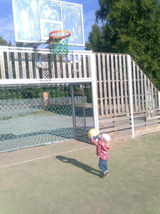 niño pequeño sosteniendo pelota que tirará hacia un aro de basquetbol muy alto