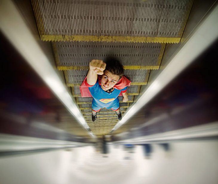 chico en escaleras eléctricas vestido de superman juega con la perspectiva