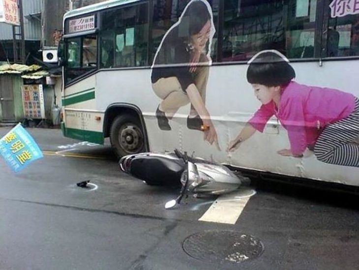 moto estrellada contra autobuz que tiene de publicidad a una señora y un niño señalando el piso