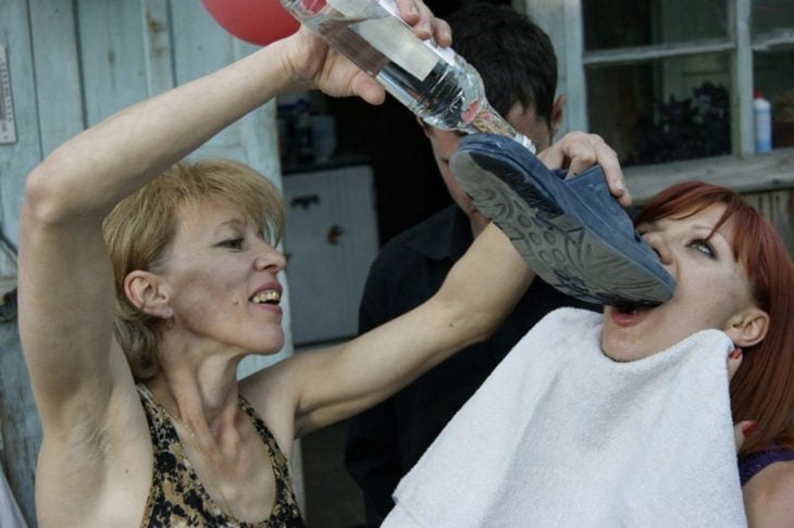 señora dando alcohol a otra mujer por medio de un zapato