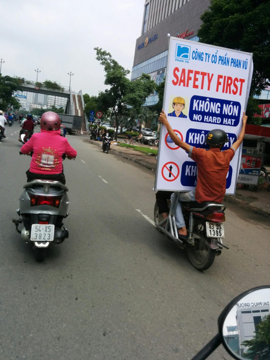 hombre de copiloto de moto cargando un enorme cartel