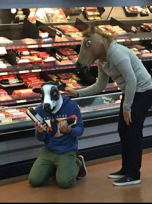 dos jovenes con máscaras de animales se lamentan en la sección de carnes frías de centro comercial