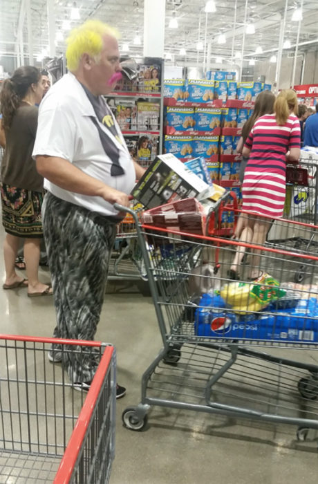 hombre con cabello amarillo y bigote rosa empuja carrito de compras