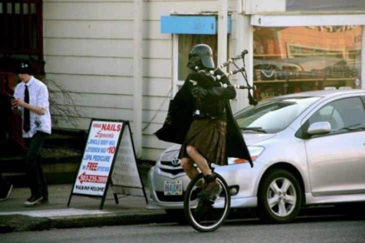 hombre en monociclo con falda escocesa y casco de darth vader 