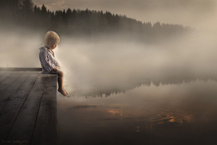 niño sentado al lado de un lago