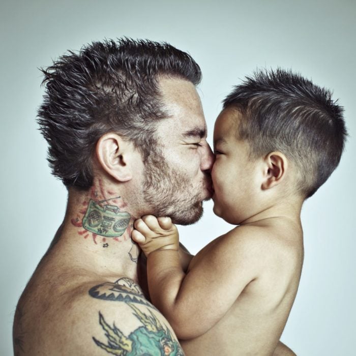 papá tatuado besa a su niño de brazos 