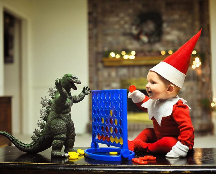 bebé vestido de elfo con godzilla de juguete