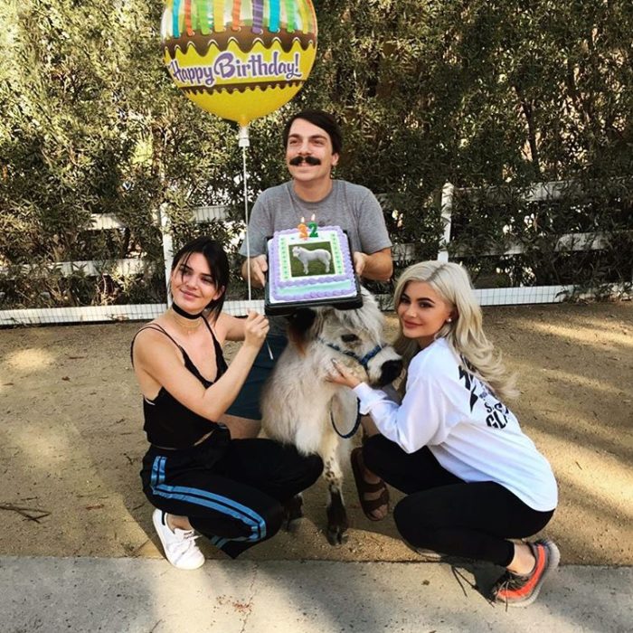 hombre se edita al lado de kendall jenner y kilye sosteniendo un pastel