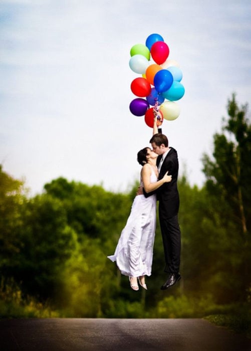 novios besándose sostenidos de globos de colores