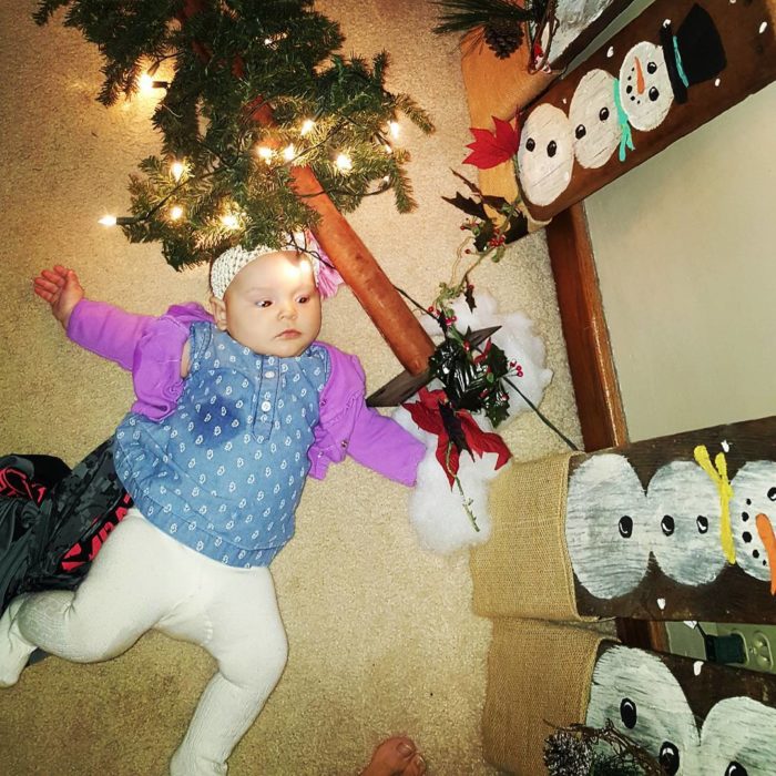 niña en el suelo con árbol de navidad tirado cerca de su cabeza