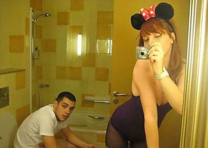 mujer con orejas d eminie mouse se toma selfie en el baño mientras un hombre está en la taza
