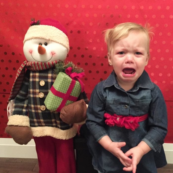 niño llorando al lado de un muñeco navideño