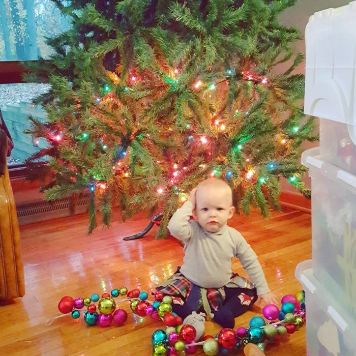 niño en el suelo frente a árboil navideño y con esferas navideñas en el suelo