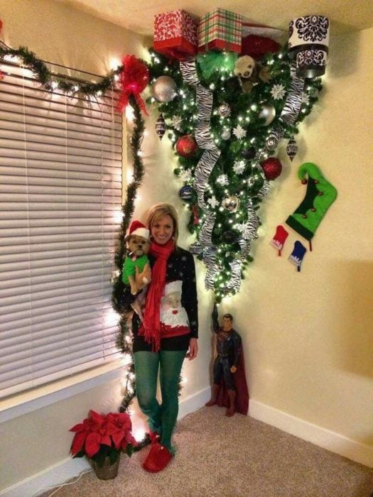 mujer posa con su perro al lado de árbol de navidad puesto de cabeza