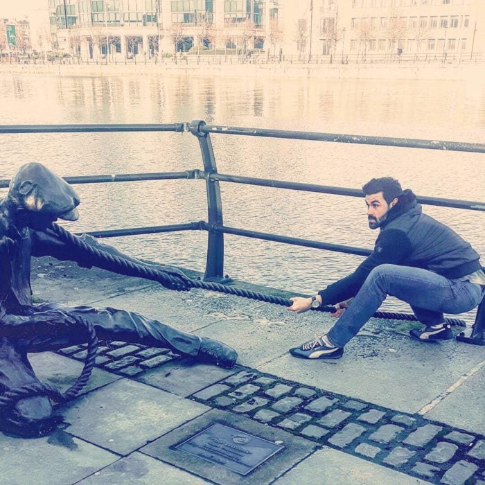 hombre posa al lado de estatua de hombrecillo que tira de una cuerda