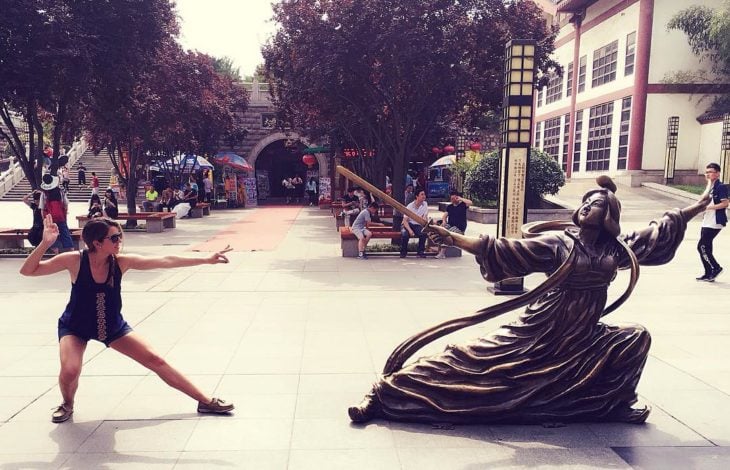 mujer posa al lado de una estatua de mujer oriental en posición de combate