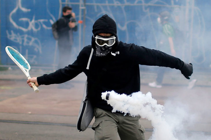 manifestante avienta un frasco de gas con una rqueta