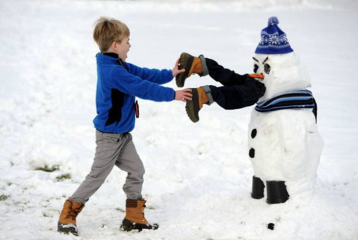 muñeco de nieve que parece que se comió a un niño mientras otro infante trata de sacarlo de su boca