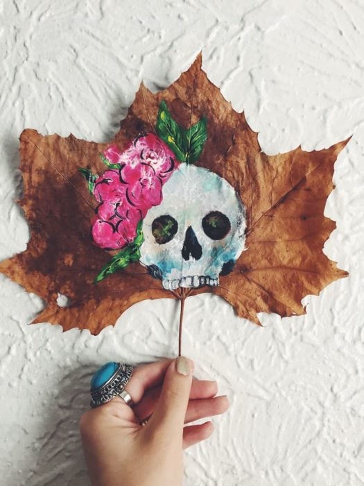 una calavera con moño pintada en una hoja de árbol 