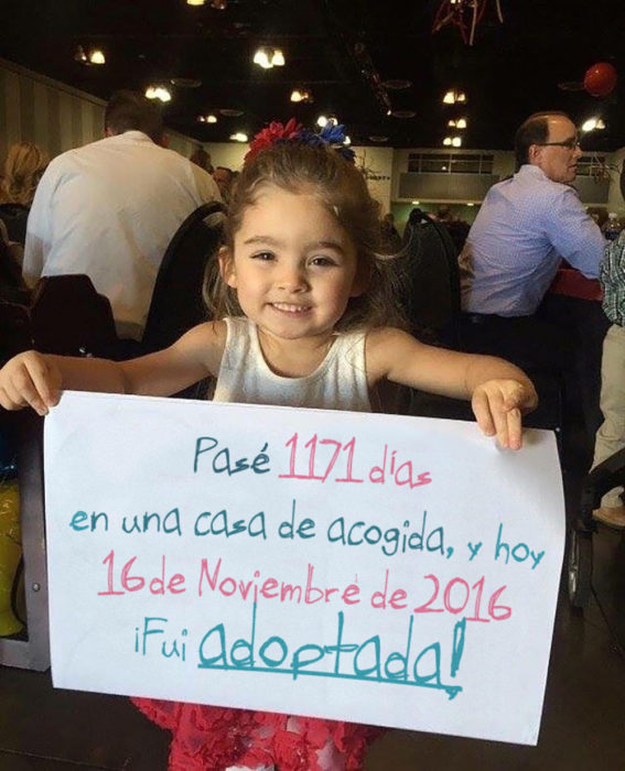 niña sosteniendo un cartel en el que dice que fue adoptada