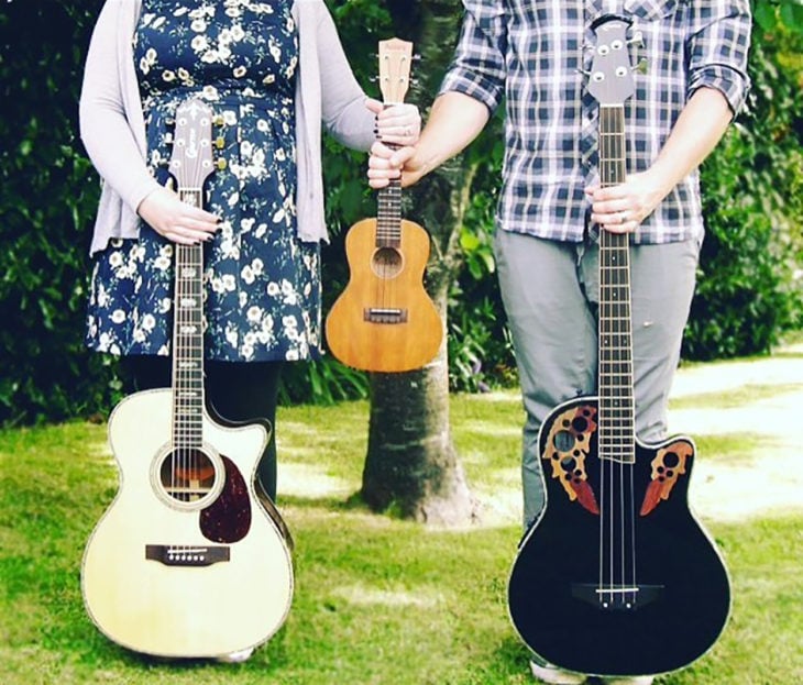 mujer y hombre sostienen en sus respectivas manos derechas guitarras y juntos con su mano izquierda una guitarrra pequeña