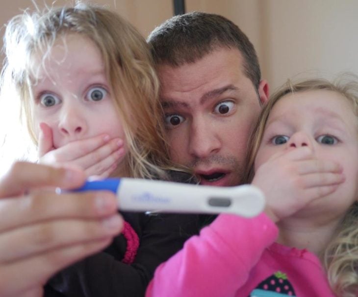 hombre con sus dos hijas pequeñas sostiene una prueba de mebarazo