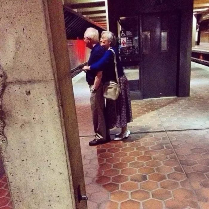 Pareja adultos mayores abrazados esperando el metro 