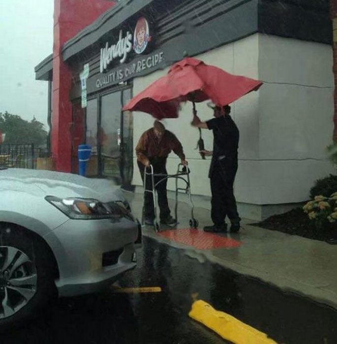 foto de trabajador de wendys que lleva una sombrilla tapando a un anciano de mojarse 