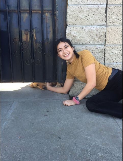 chica se toma foto mientras acaricia a perro por la rendija de un portón
