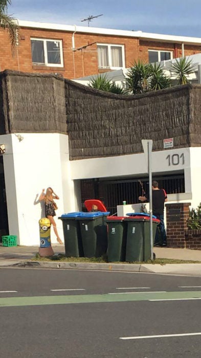 hombre tomando fotos a mujer al lado de botes de basura