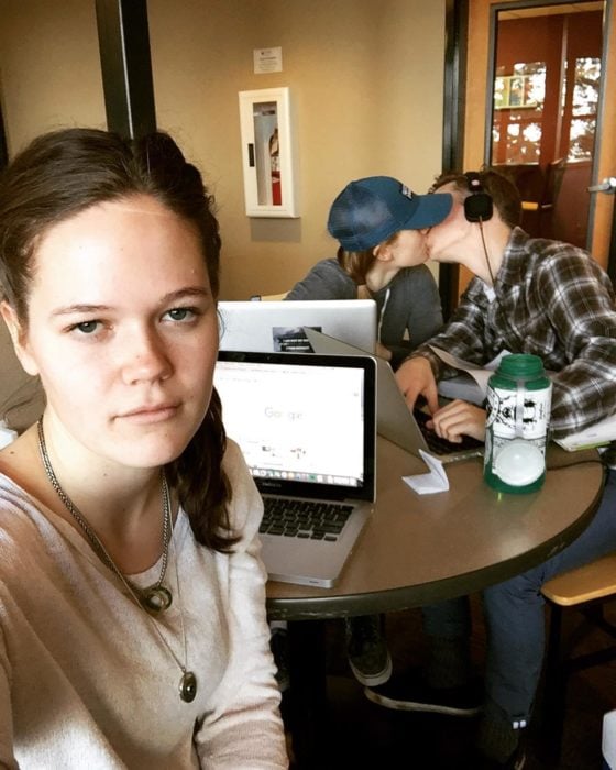 muchacha con laptop frente a una pareja que se besa en una cafetería