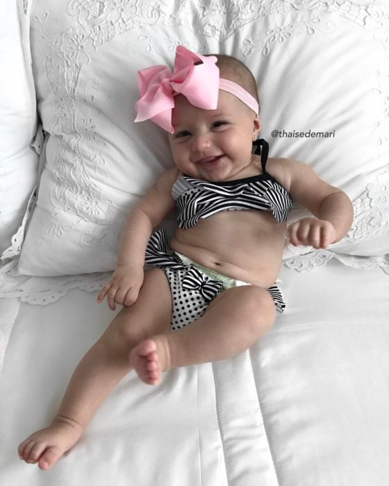 bebé sonriendo con bikini y moño rosa