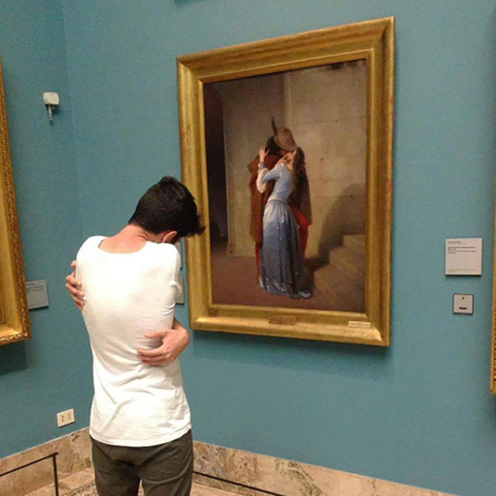 muchacho abrazándose a sí mismo frente a un cuadro de romeo y julieta