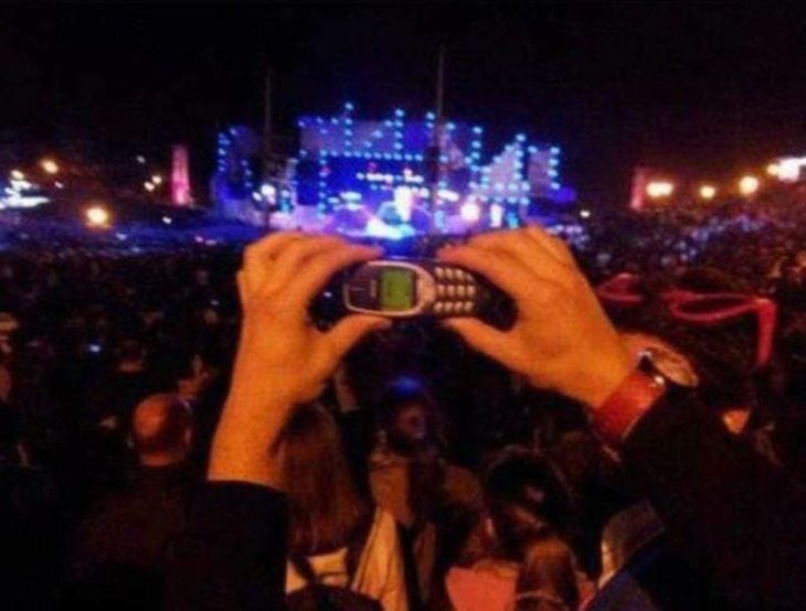 hombre sosteniendo un celular antiguo en un concierto