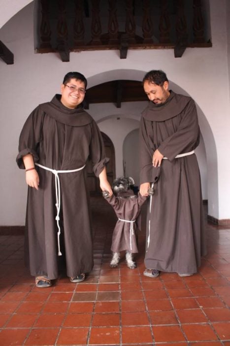 dos franciscanos tomando de las patitas a un perro con hábito