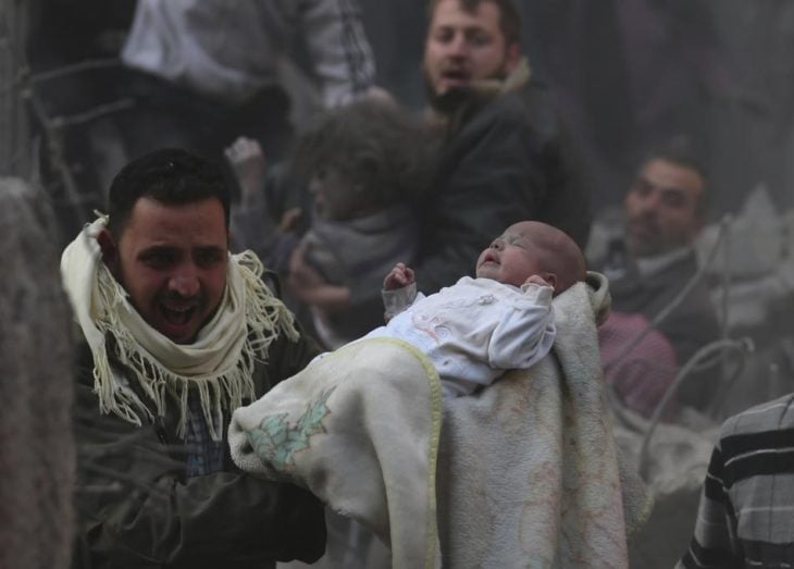Hombre carga a bebé que sobrevivió a un ataque en Siria
