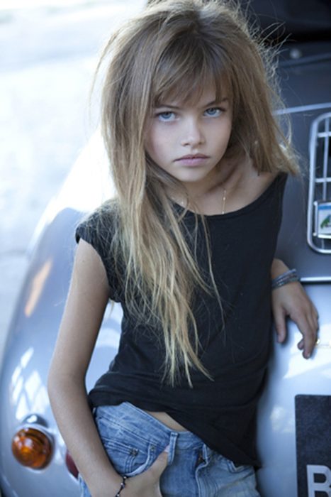 niña recargada en coche con el cabello despeinado